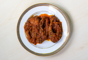 Spicy rui fish curry or rui mach bhuna in a white plate on light wooden surface.