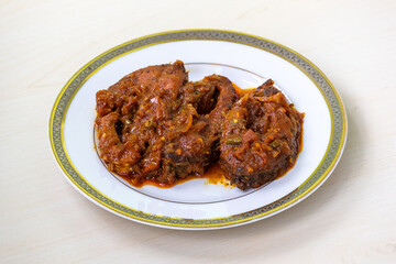Delicious rui fish curry or rui mach bhuna in a white plate on light wooden surface.