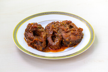 Rui fish bhuna or curry in a white plate on light wooden surface. Traditional Bengali food or cuisine.