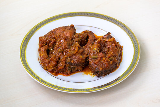 Delicious rui fish curry or rui mach bhuna in a white plate on light wooden surface.