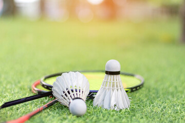 Badminton sport equipments, rackets and white feather shuttlecocks, on green grass lawn, soft focus.