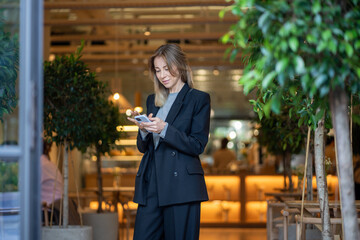 Interested businesswoman stands with smartphone look at screen reads email, message, examines...