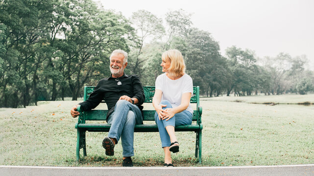 Happy senior couple sitting on bench in the park with legs crossed in park nature. Healthy and happy retirement concept