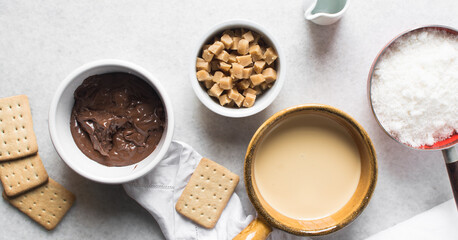 Overhead view of mise en place for making chocolate fudge with cookies and fudge pieces, Top view of ingredients of hazelnut chocolate fudge, process of making chocolate fudge