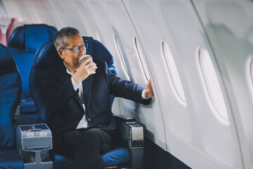 Attractive Asian male passenger of airplane sitting in comfortable seat while working laptop and tablet with mock up area using wireless connection. Travel in style, work with grace.