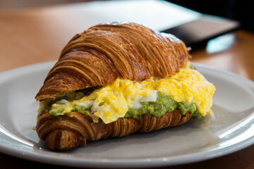 Breakfast of coffee with milk, croissant with guacamole and scrambled egg, poached egg, butter in a...