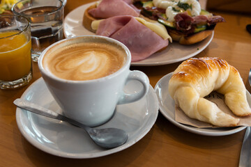Breakfast of coffee with milk, croissant with guacamole and scrambled egg, poached egg, butter in a roll, ham and cheese, avocado and bacon