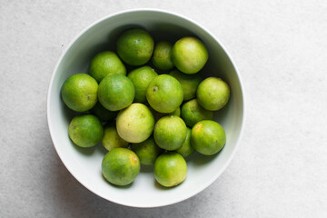 Overhead view of green limes in a white ceramic bowl, top view of organic limes in a white bowl