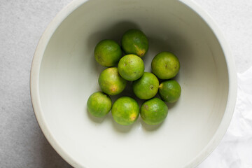 Overhead view of green limes in a white ceramic bowl, top view of organic limes in a white bowl