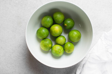 Overhead view of green limes in a white ceramic bowl, top view of organic limes in a white bowl