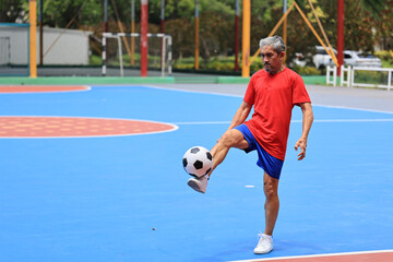 Senior Asian man in retirement age playing soccer football at outdoor court for healthy and fun...
