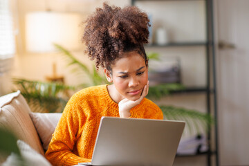 African american Afro haired woman studying at home using a computer laptop serious face thinking...