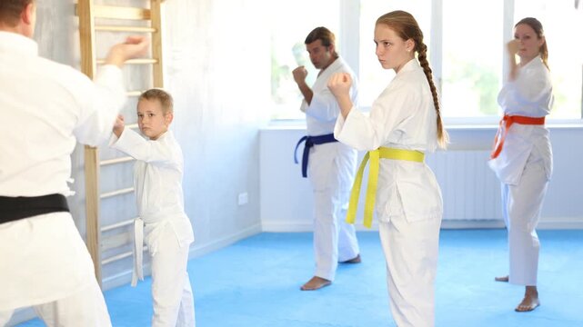 Teen girl and her family repeat movements and learn fighting techniques during martial arts lesson. Experienced man unrecognizable instructor conducts personal karate training for large family