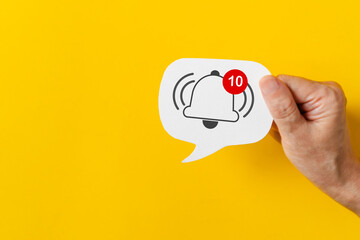 Hand hold  real white speech bubble paper cut with alert sign, conversational cloud and a bell icon for internet channel subscription symbol and a subscription reminder