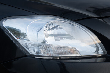 Close up used headlights of luxury black car. Environment of car in the dark tone.
