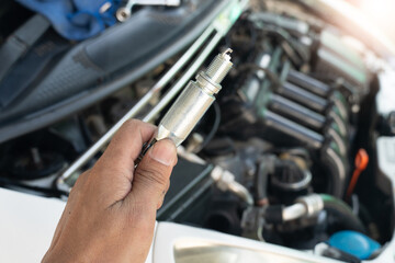 Car mechanic hand holding spark plug to repair car engine in garage. A set of socket wrenches to...