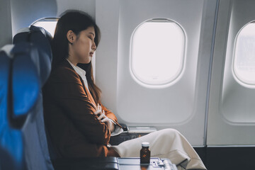 Fototapeta premium Photo of a frustrated woman sitting on an airplane with her head in her hands. Asian woman sitting in a seat in airplane