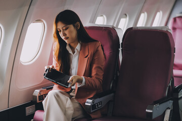 Attractive Asian female passenger of airplane sitting in comfortable seat while working laptop and...