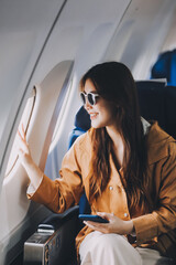 Joyful asian woman sits in the airplane and using tablet while go to travel