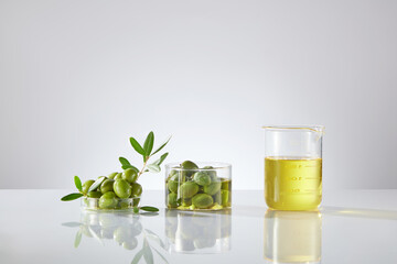 On the light background, laboratory dishes and flasks containing fresh olive and olive oil. Front view, natural ingredient for cosmetic product. Olives contain many healthy nutrients