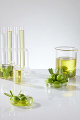Fresh olives and olive oil contained on beakers, petri dishes and test tube decorated on white background. Lab theme for advertising product with olive oil extract