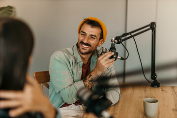 Two cheerful radio hosts in headphones recording podcast in broadcasting. Focus on a male guest...