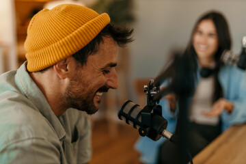 People in the podcast studio talking and recording. Focus on a smiling man with a yellow cap