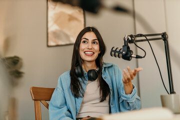 Confident Latin woman with headphones and microphone recording a podcast at home