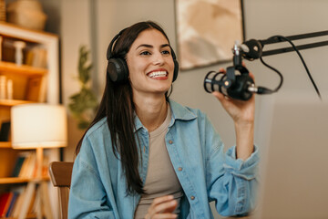 A young female influencer with headphones online live talking to the audience using microphone and...