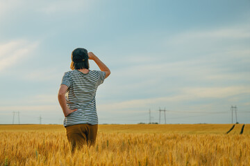 Female farmer standing in ripe wheat field and looking over the harvest ready crops at the horizon and sunny sky