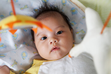 asian cute innocent baby newborn boy looking and play at the mobile hanging toy on the fabric crib...