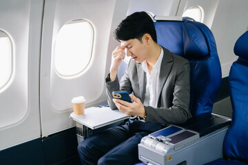 Obraz premium Photo of a frustrated man sitting on an airplane with her head in her hands. Asian Businessman sitting