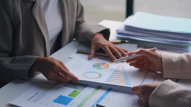 Business professionals analyze financial charts and discuss graphs at a meeting table. In depth examination of business data and collaborative decision making in a contemporary office setting