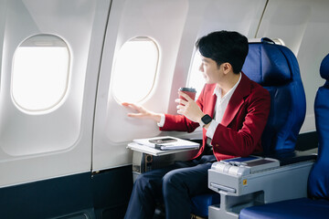 Young Asian executive excels in first class, multitasking with digital tablet, laptop and...