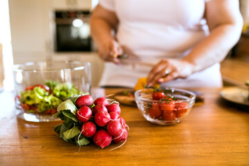 Overweight woman in the kitchen, making homemade lunch. Choosing healthy food, making and eating vegetable salad.