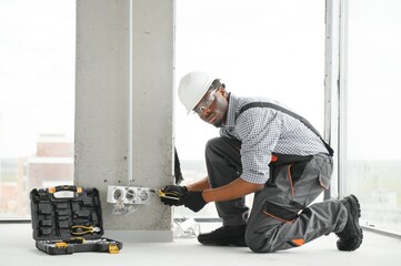 An African electrician installs electrical outlets at a construction site
