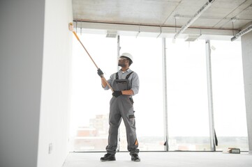 African man paints a white wall with a roller. Repair of the interior