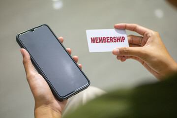 close up of woman's hand holding membership card, or mockup card. paying with membership card. with mobile phone beside card.