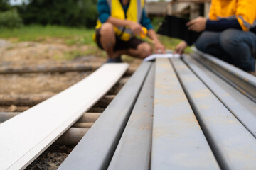 Two men, engaged in conversation, examine steel reinforcements and discuss the house structure and roofing. As contractors, they focus on ensuring quality and safety in the construction work.