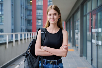 Outdoor portrait young teenager student blonde female with backpack, urban style background