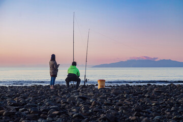 People fishing along the shoreline of the Firth of Thames at sunset at Orere Point, Auckland, New...