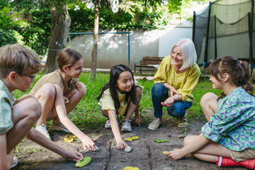 Students playing tic-tac-toe with stones and leaves, grid in soil. Outdoor sustainable education class.