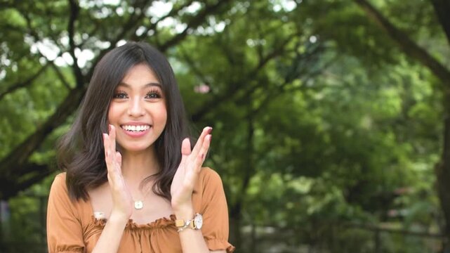 A young woman is shocked and overjoyed after being told good news. Covering her mouth, feeling giddy. Outdoor park scene. Slowed down 50 percent.