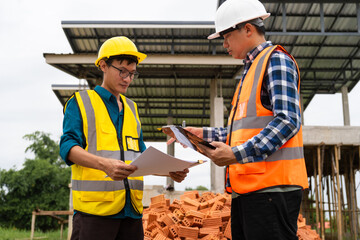 Two male architects wearing hard hats and safety vests discuss construction design...