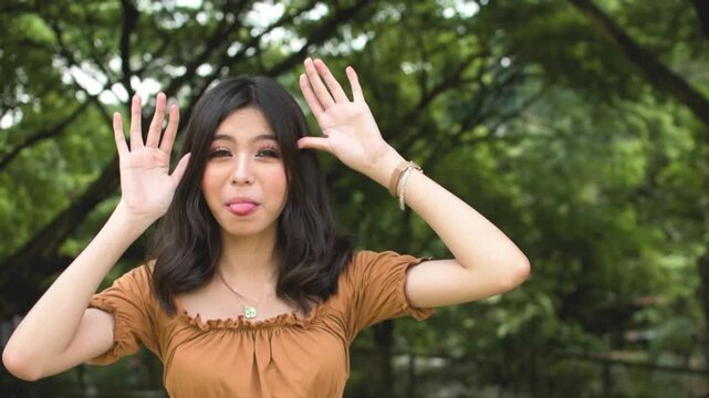 A young asian woman teasing someone by sticking out her tongue. Taunting a friend but in a playful manner. Outdoor park scene. Slowed down 50 percent.