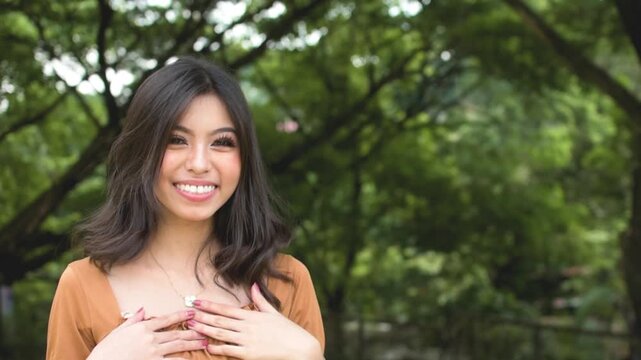 A friendly young asian lady introduces herself then offers a handshake. Bubbly lady establishing rapport. Outdoor park scene. Slowed down 50 percent.