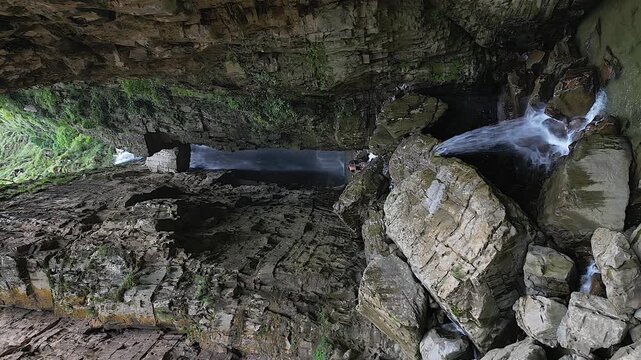 Vertical format aerial pull-in to waterfall in narrow rock cliff gorge