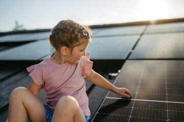 Cute girl on roof with solar panels, standing with open arms, hands up in the air. Rooftop solar or photovoltaic system. Sustainable future for next generation.