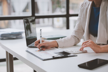 Asian female finance staff is pressing a calculator to calculate company sales and profit to report her boss, profit calculation idea. And the company's performance