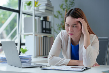 Asian businesswoman sitting in office stressed and fatigued from overwork on financial matters on office desk.